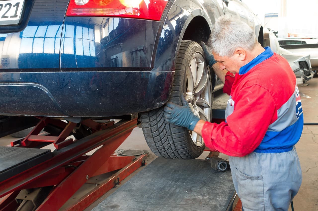 A car raised on a scissor lift while a mechanic checks the rear wheel and tyre